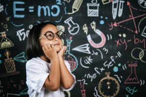 Portrait of happy little schoolchild wearing eyeglasses on background of backboard in school, smile and looking to camera in funny gesture